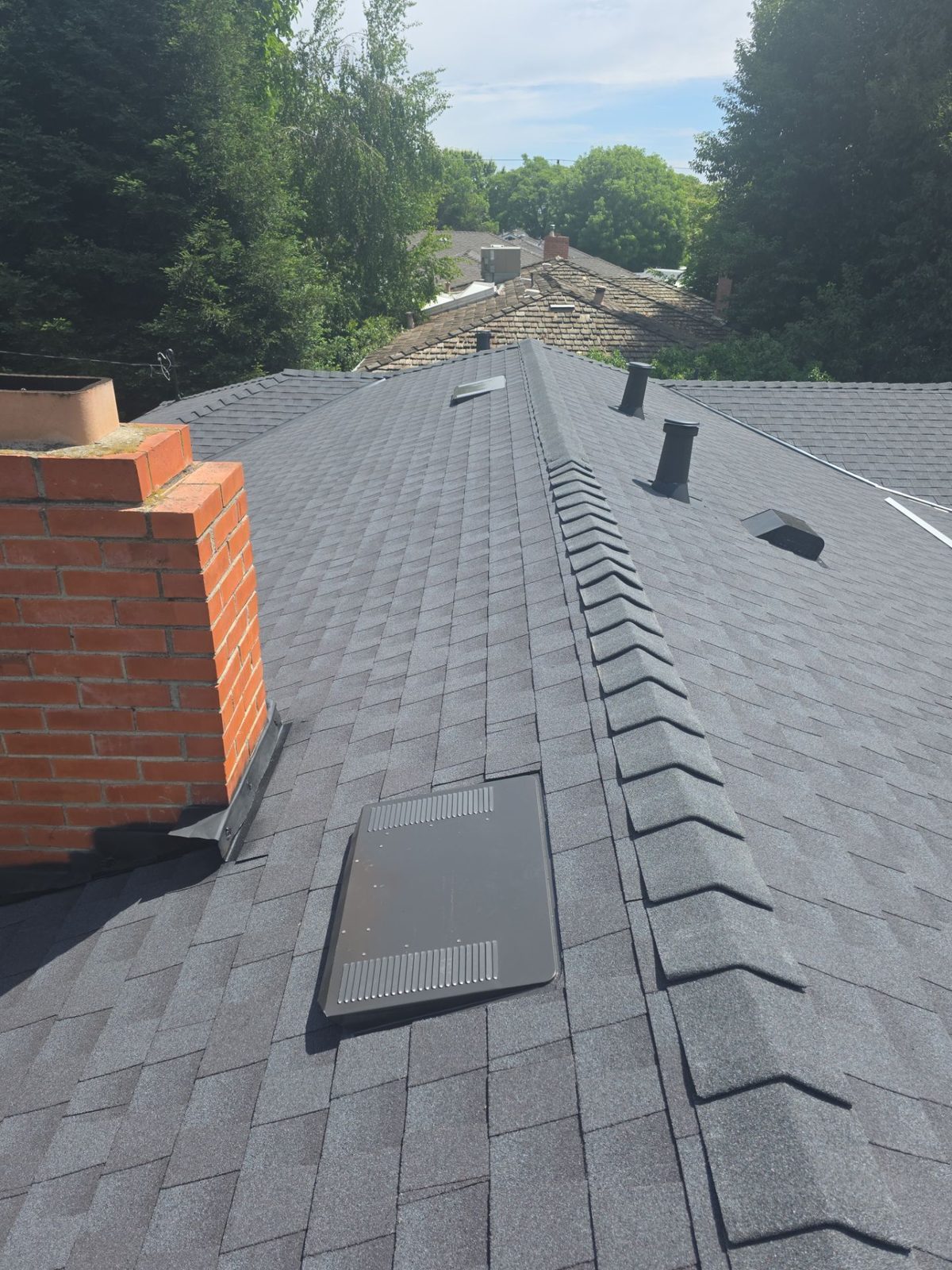 New ridge cap and vents beside the brick chimney on a finished Turlock roof