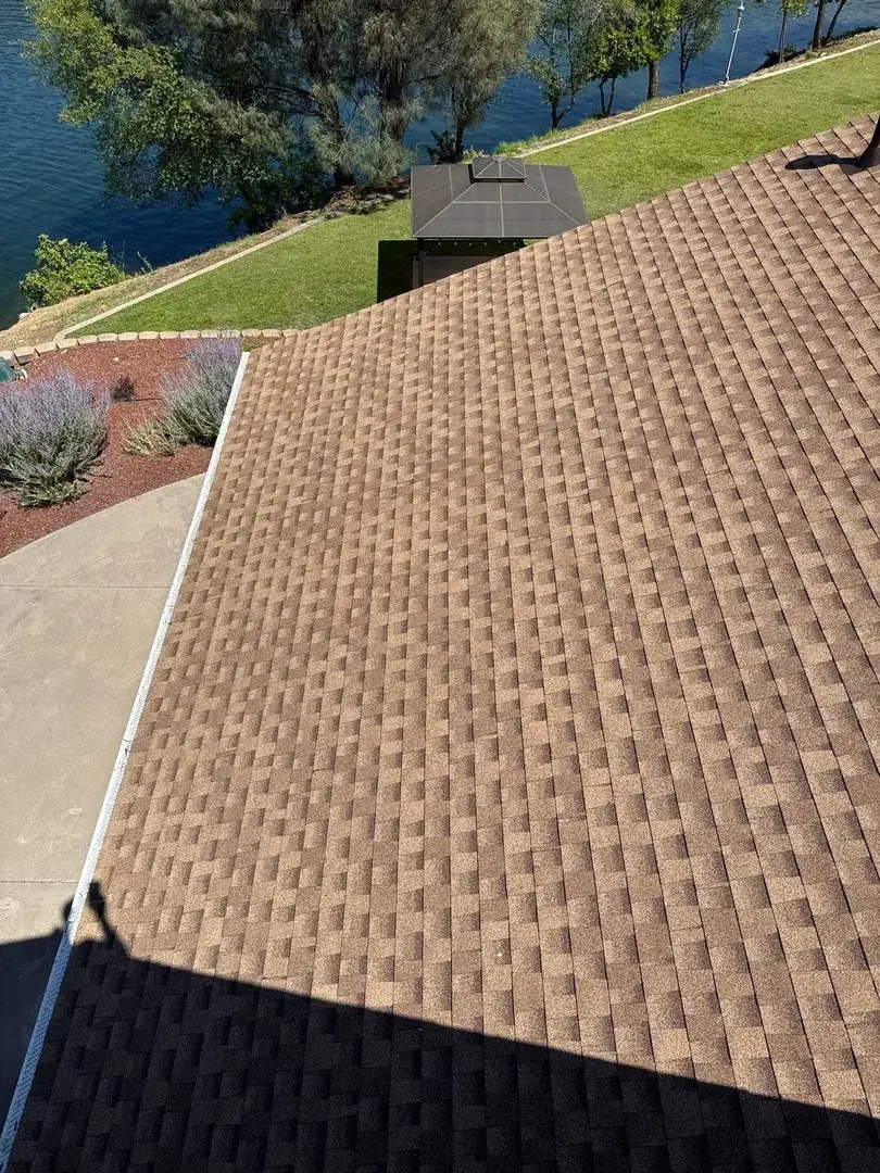New brown architectural shingles and a clean gutter line with gutter guards above the landscaped yard at the Jamestown home